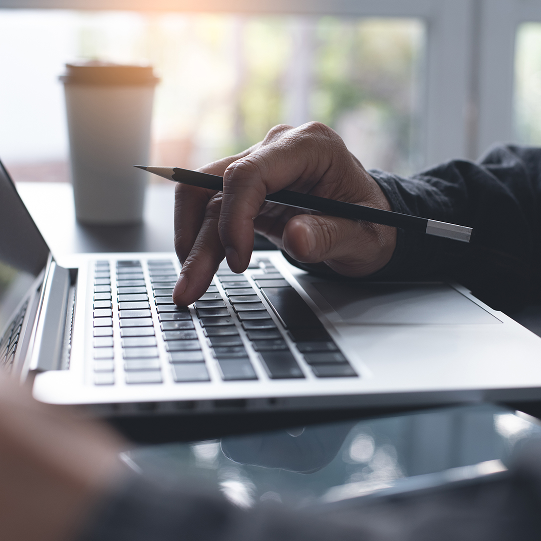 Closeup of business man with pencil in hand typing on laptop computer keyboard, searching internet while online working at modern home office with cup of coffee, mobile smart phone on table and morning light